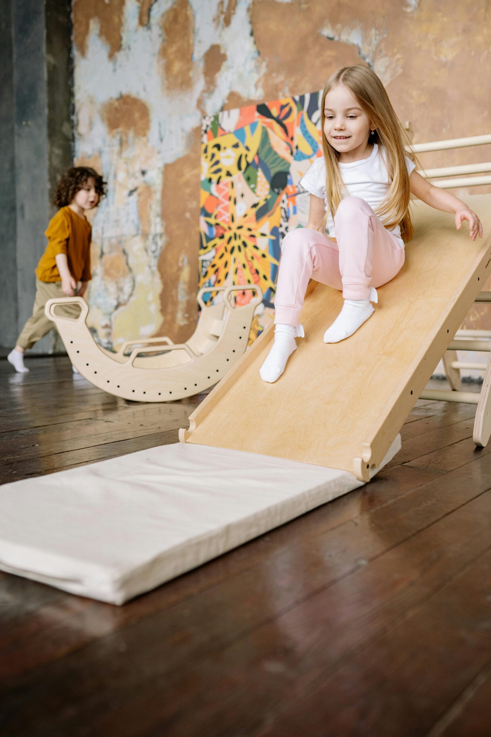 Happy children playing on a wooden slide indoors, enjoying their playful moment.