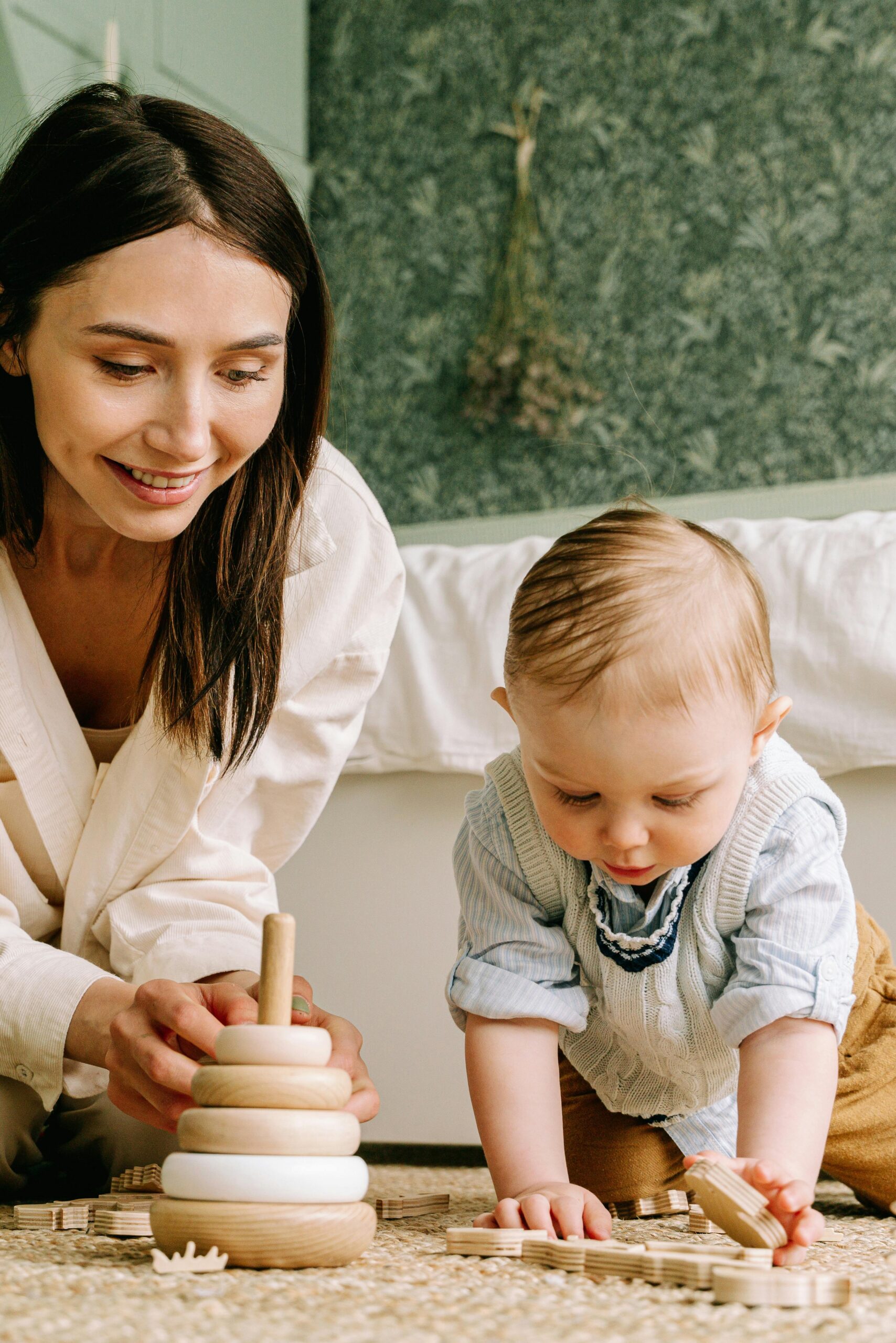 A mother and her baby joyfully playing with wooden toys inside a cozy room.